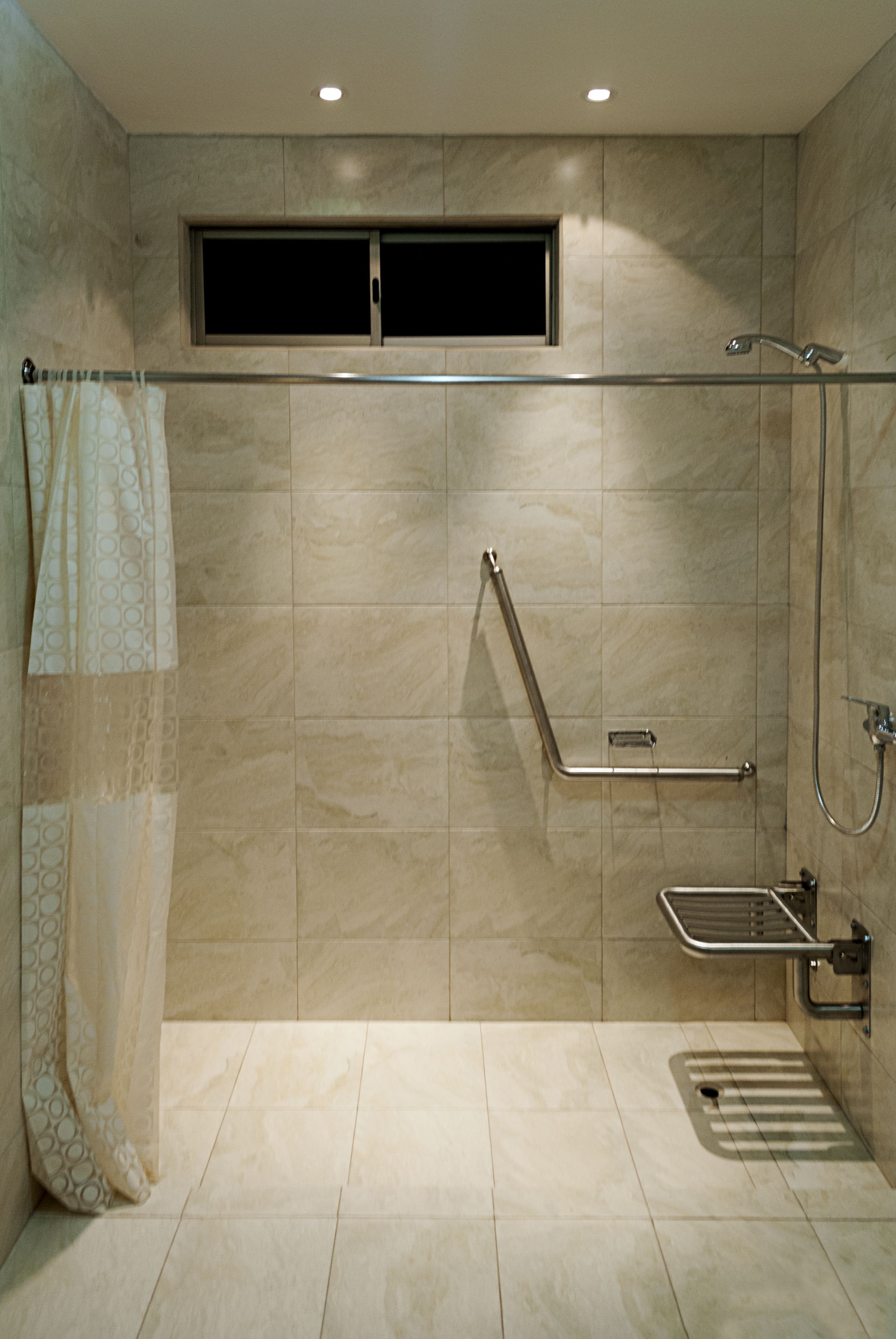 Un baño moderno con ducha, barras de apoyo y ventana.