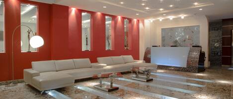 A modern lobby with a white sofa, a reception desk, and a large mirror.