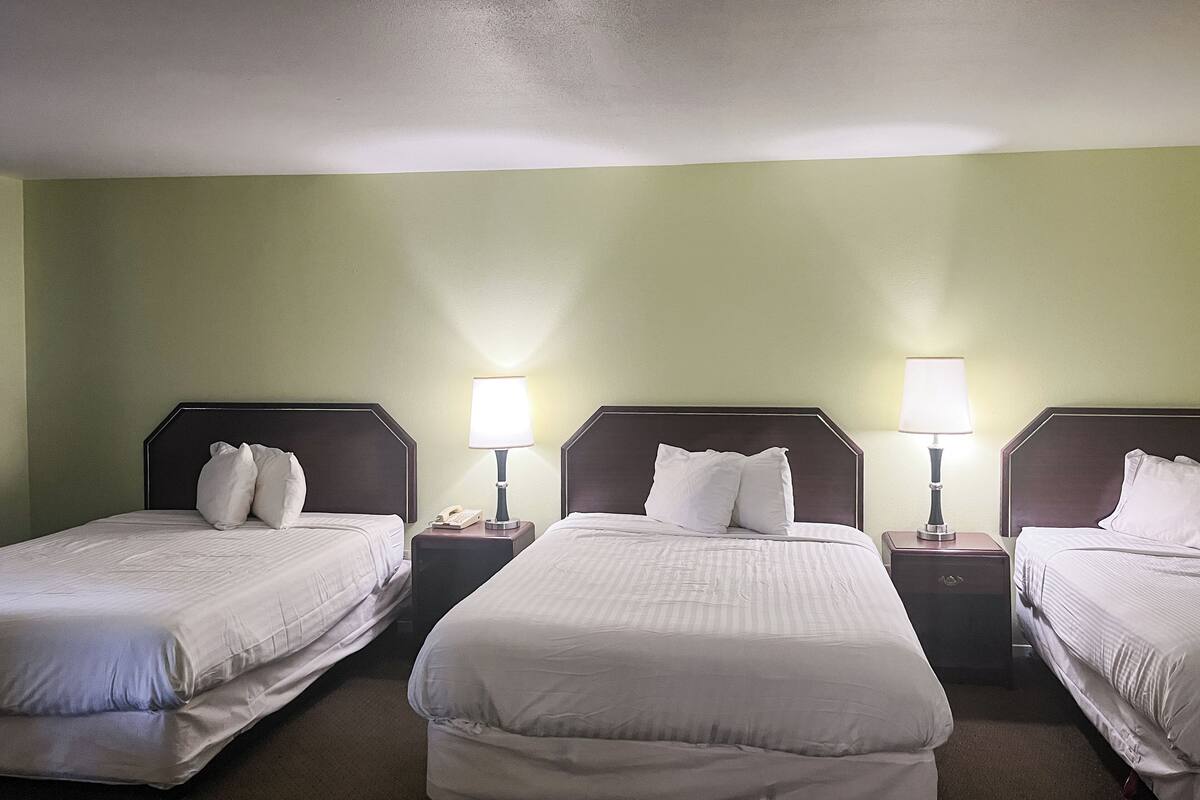 A hotel room with three beds, each with a nightstand and a lamp.