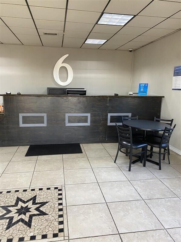 A reception area with a large number '6' on the wall, a reception desk, a black rug, a tiled floor with a star pattern, and a table with chairs.