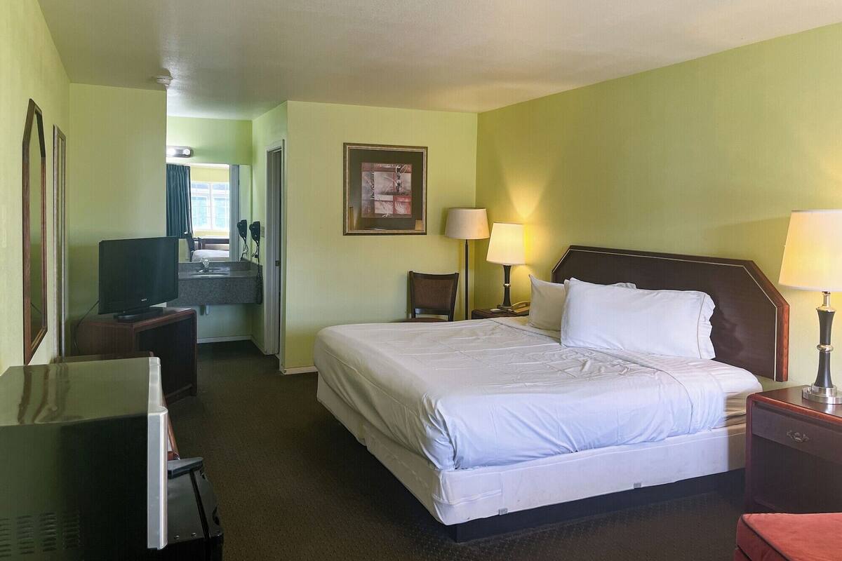 A hotel room with a bed, two bedside lamps, a television, a desk, and a mirror.