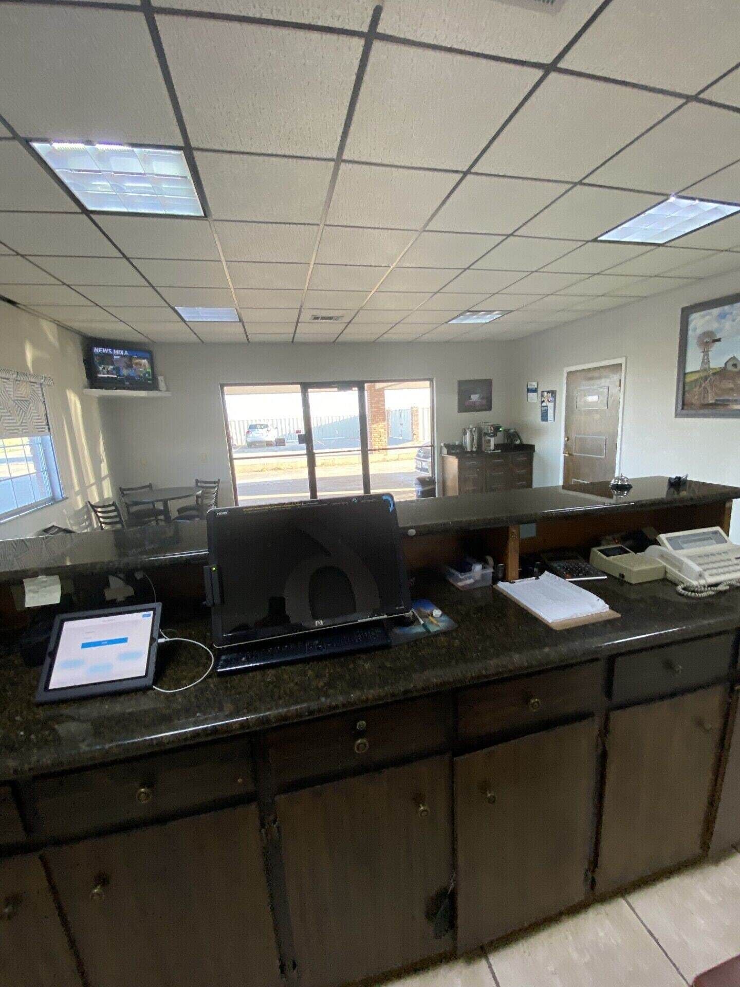 Zona de recepción con mostrador, computadora, teléfono y televisor mostrando noticias.