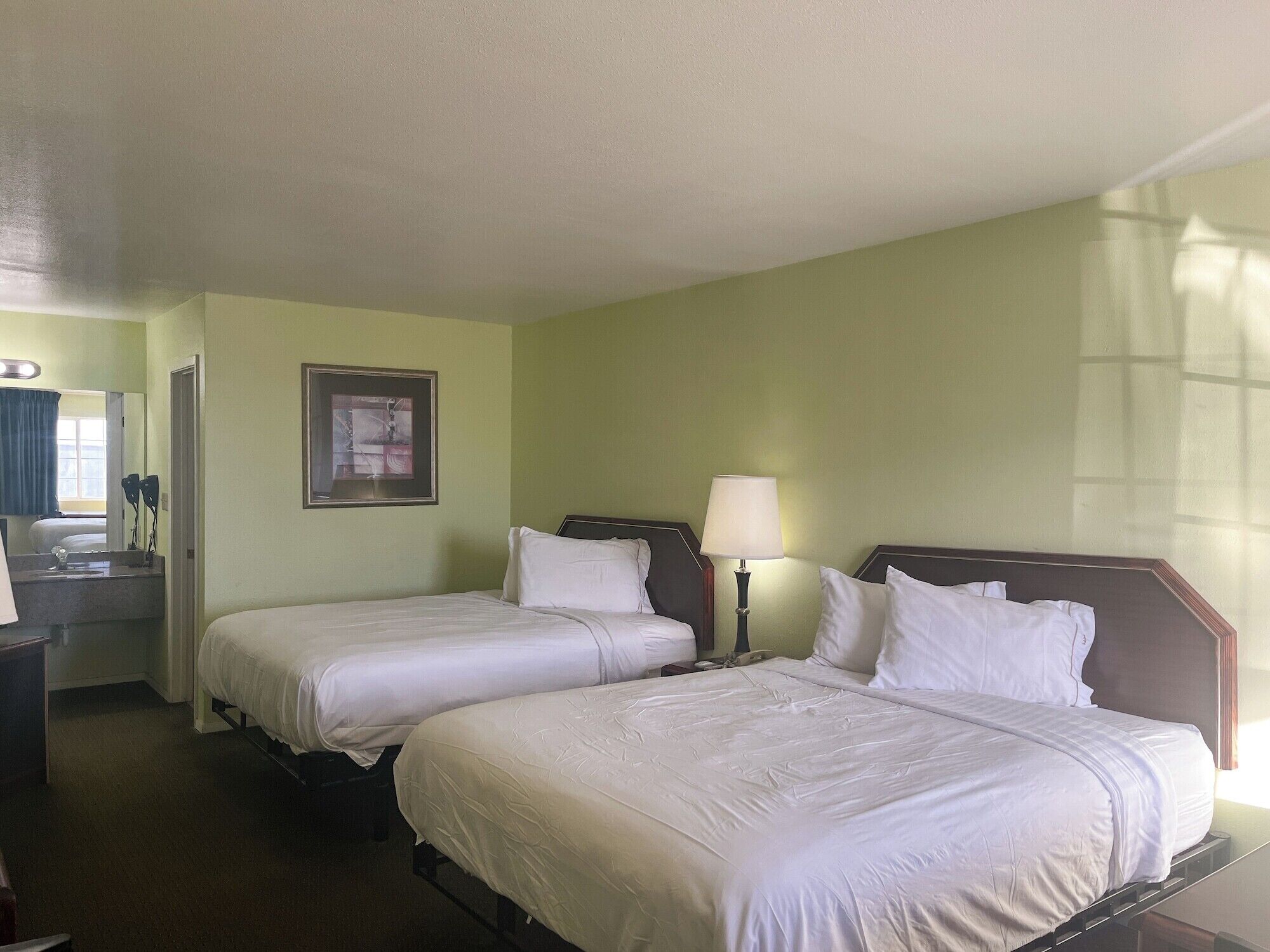 Habitación de hotel con dos camas, un escritorio, una silla, una lámpara y un cuadro en la pared.