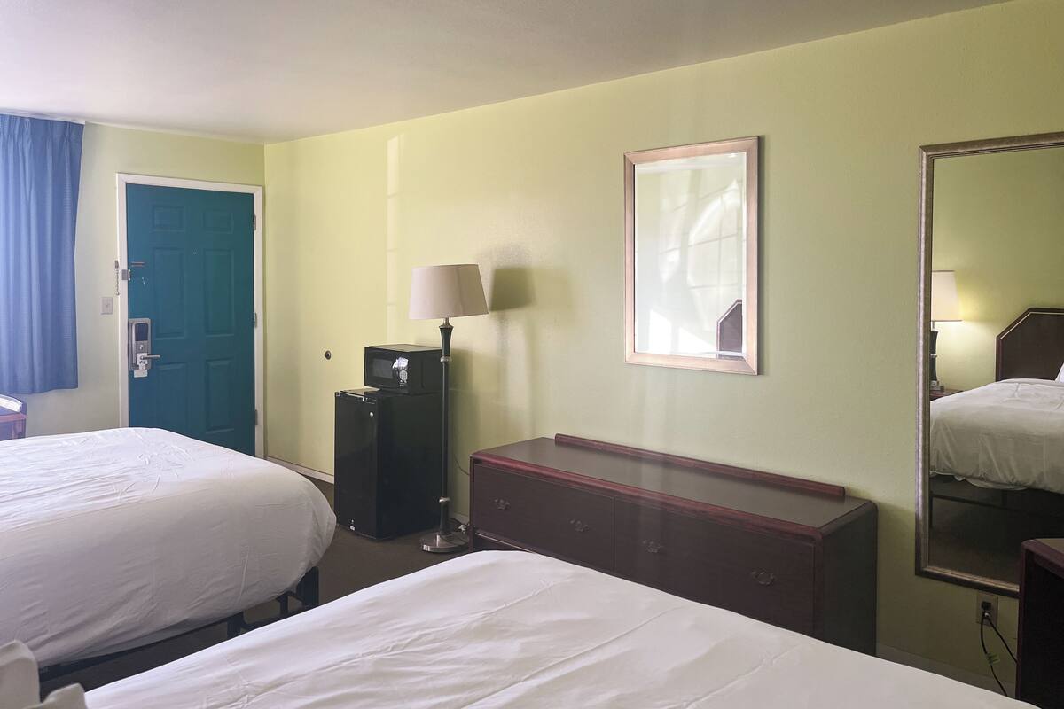 A hotel room with two beds, a desk, a dresser, a mirror, and a door.