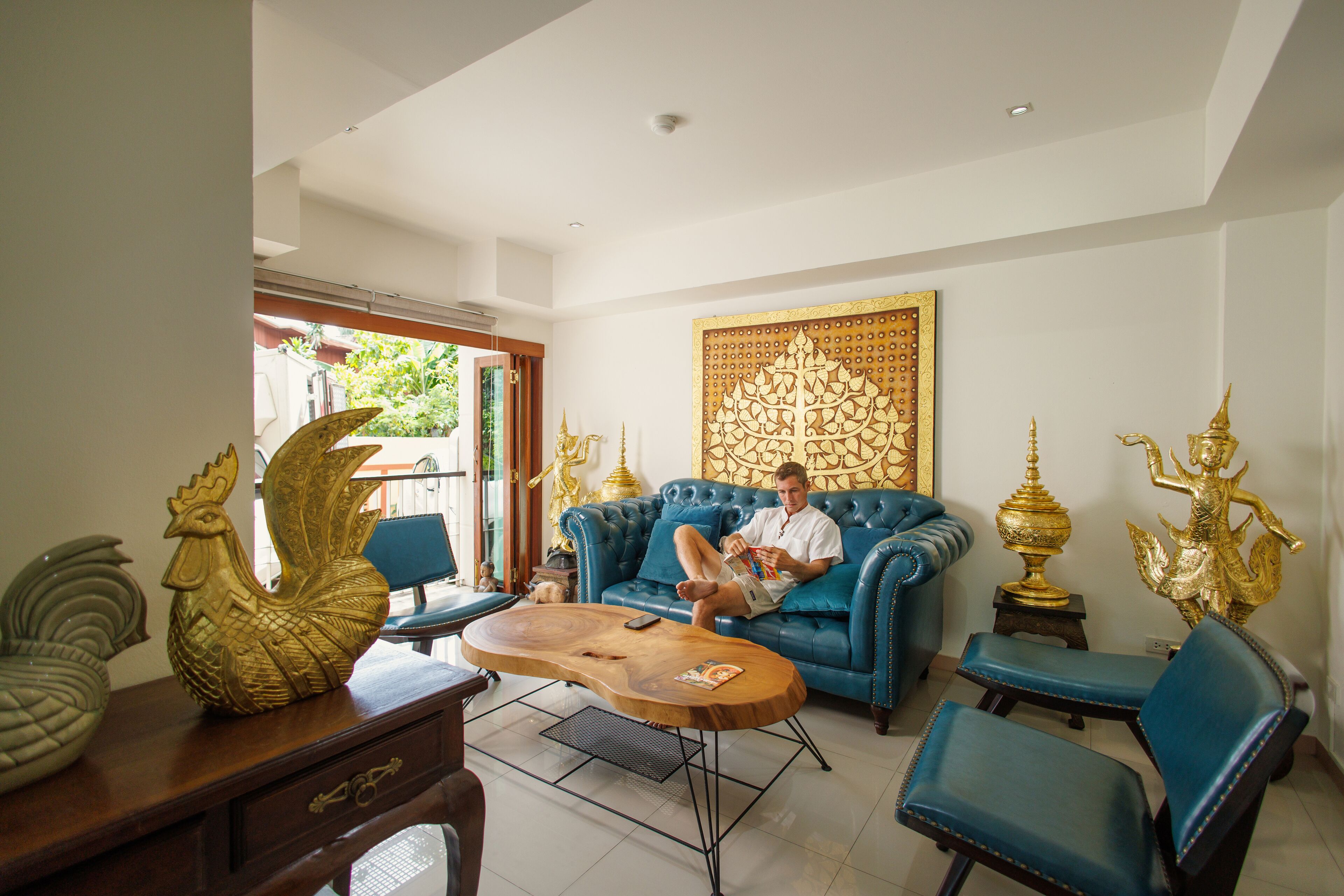 Una habitación con un sofá azul, una mesa de centro de madera y estatuas doradas decorativas.