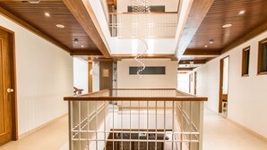 Un pasillo amplio con techo de madera, una escalera central con barandilla de metal y un entresuelo con una lámpara decorativa.