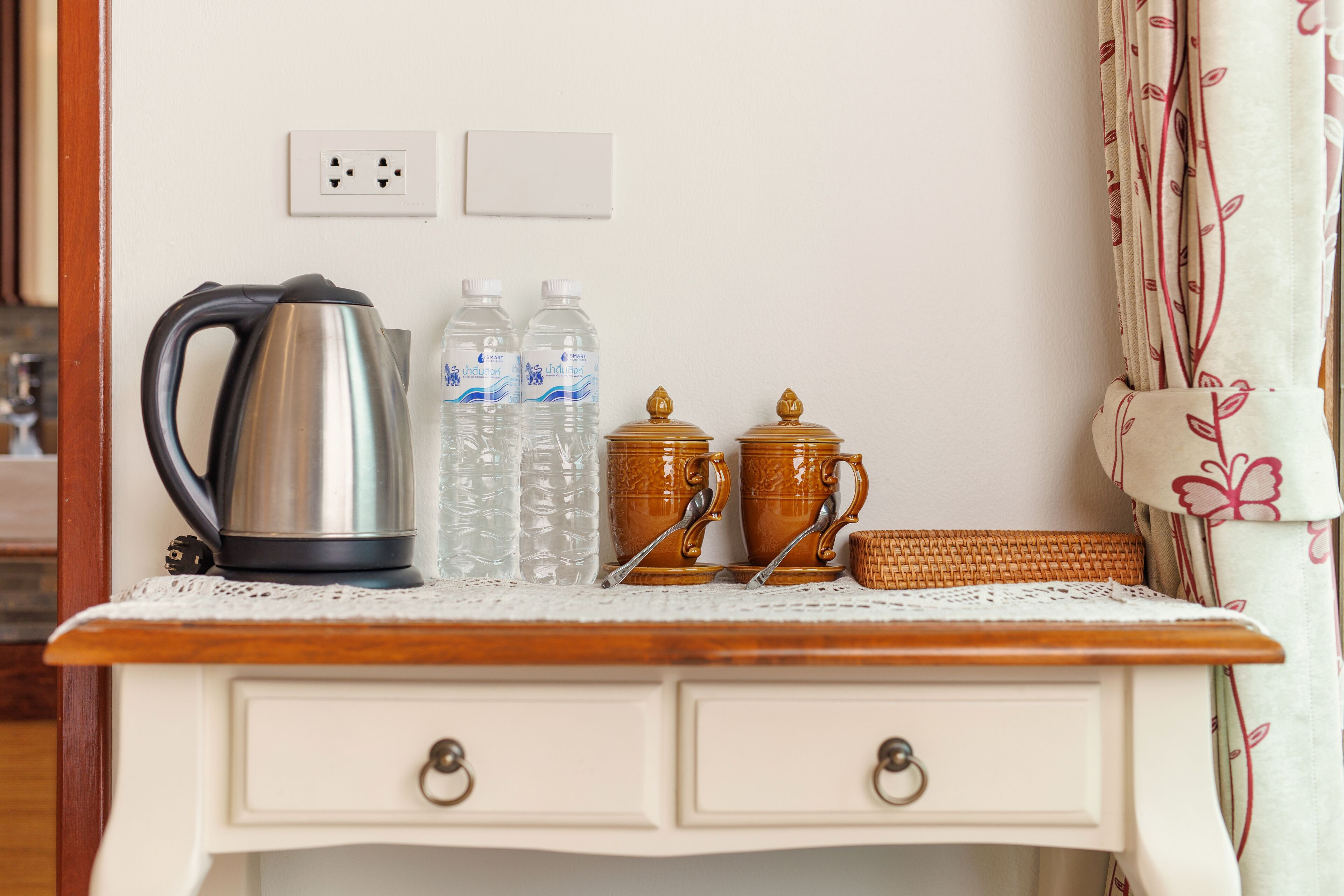 A kitchenette with a kettle, water bottles, and two ornate containers on a wooden countertop.