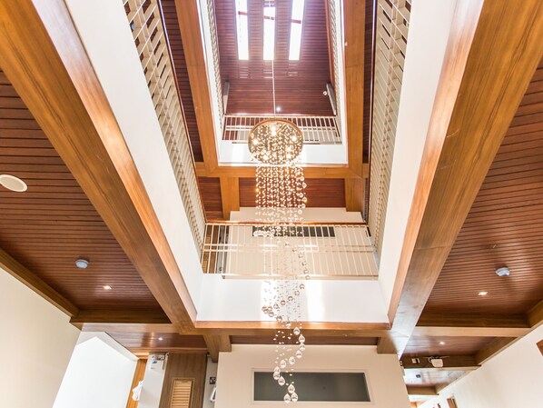 Un interior de varios niveles con vigas de madera, una lámpara colgante en el centro y una escalera.