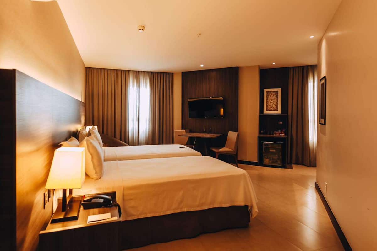 Ein Hotelzimmer mit zwei Betten, einem Schreibtisch, einem Fernseher und einer Minibar.