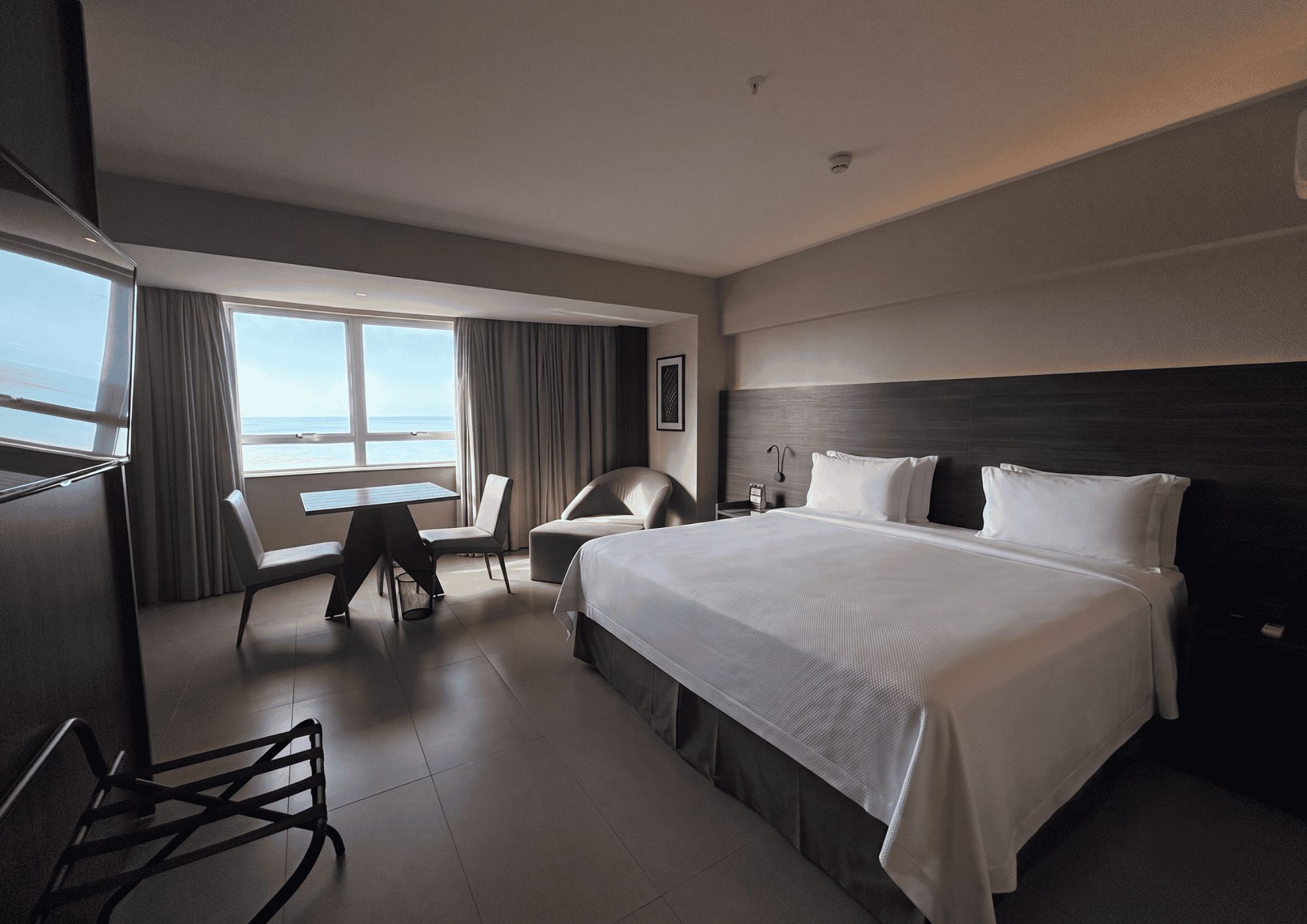 A hotel room with a large bed, a desk, a chair, and a view of the sea.