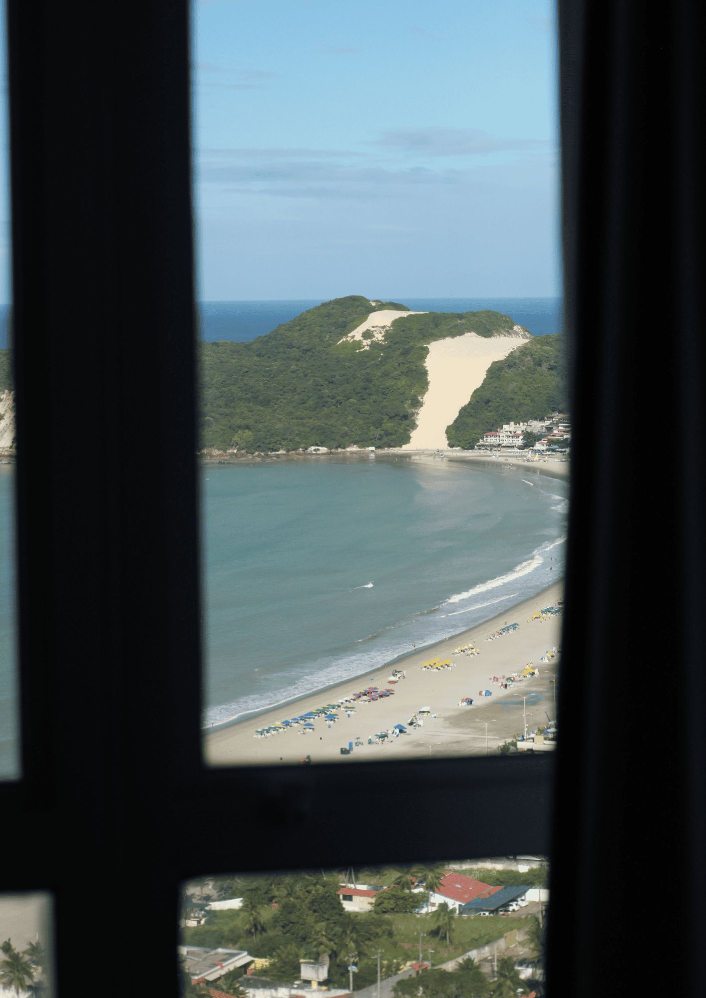 A beach with a sandy area and a forested hill in the background.