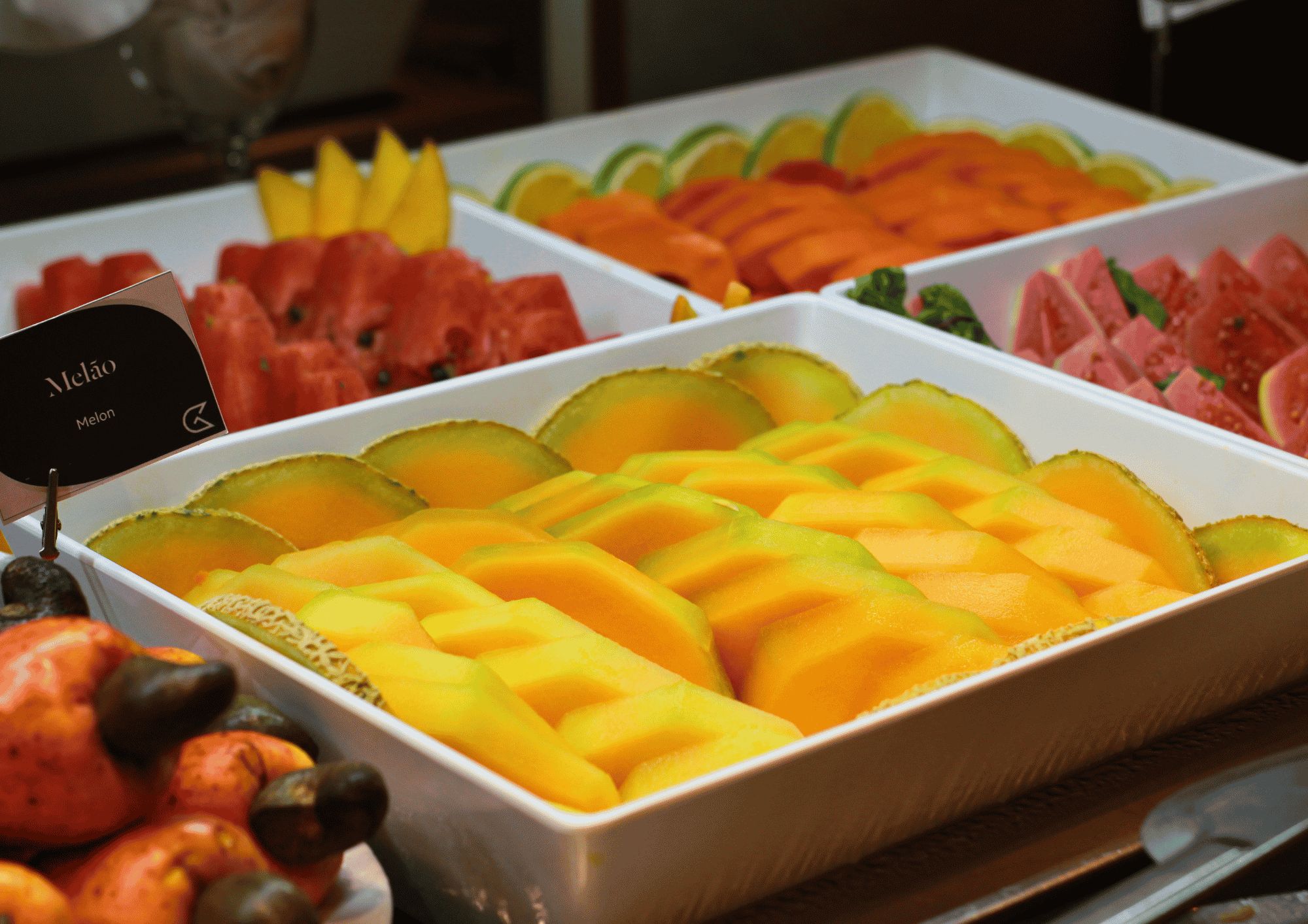 Ein Buffet mit verschiedenen Früchten und einem Schild, das 'Melão' – Portugiesisch für 'Melone' – ausweist.