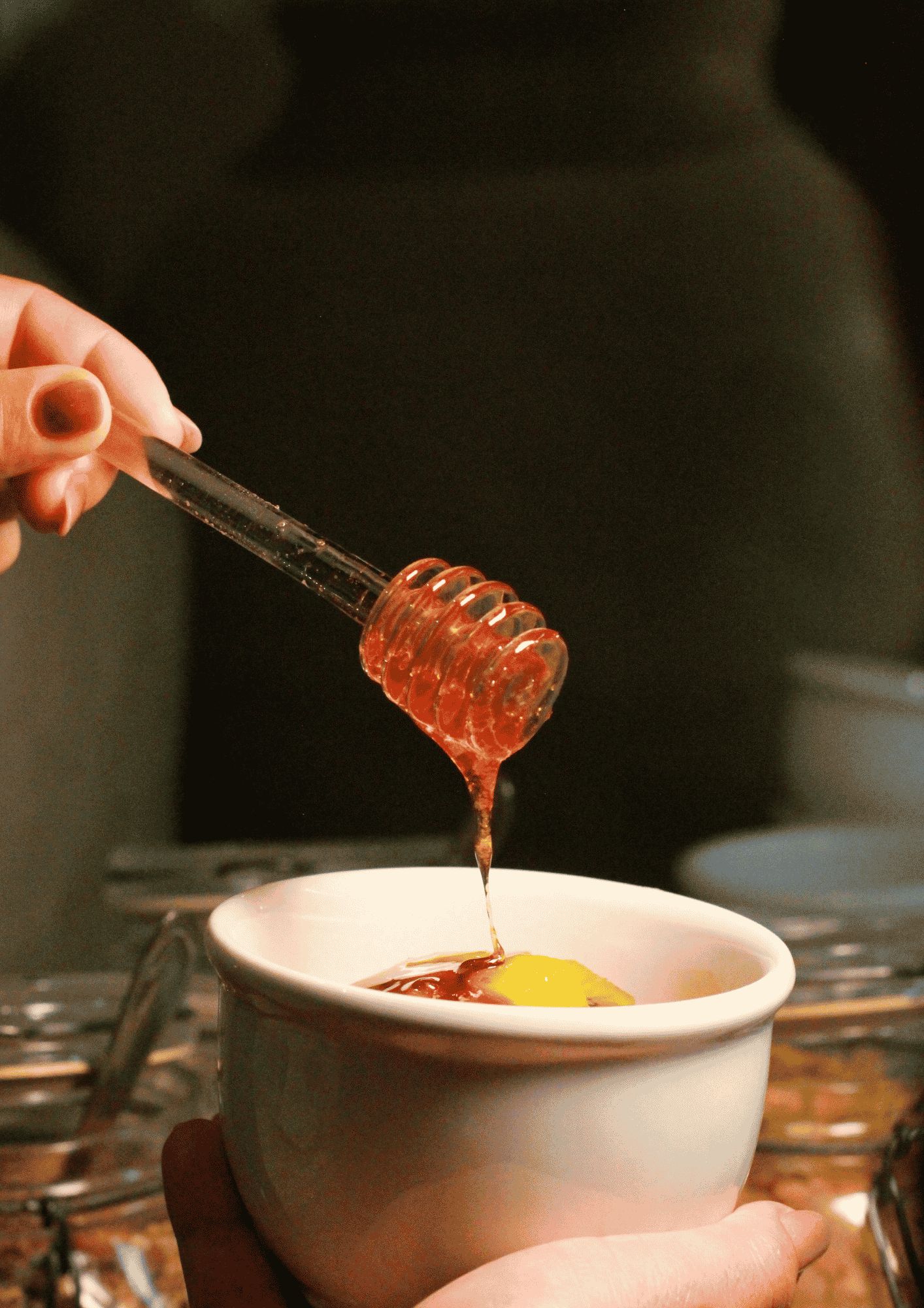 A hand holding a honey dipper over a white bowl.