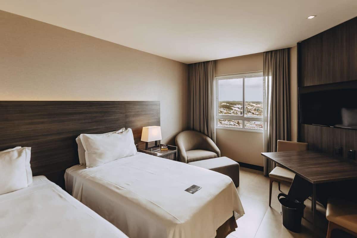 Ein Hotelzimmer mit zwei Betten, einem Schreibtisch, einem Stuhl, einem Fernseher und einem Fenster mit Blick.