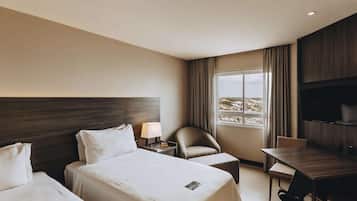 Habitación de hotel con dos camas, un escritorio, una silla, un televisor y una ventana con vistas.