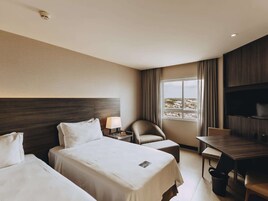 Habitación de hotel con dos camas, un escritorio, una silla, un televisor y una ventana con vistas.