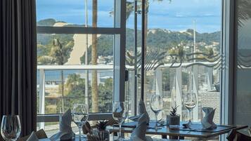 A dining area with tables set for two, overlooking a scenic view of palm trees and hills.