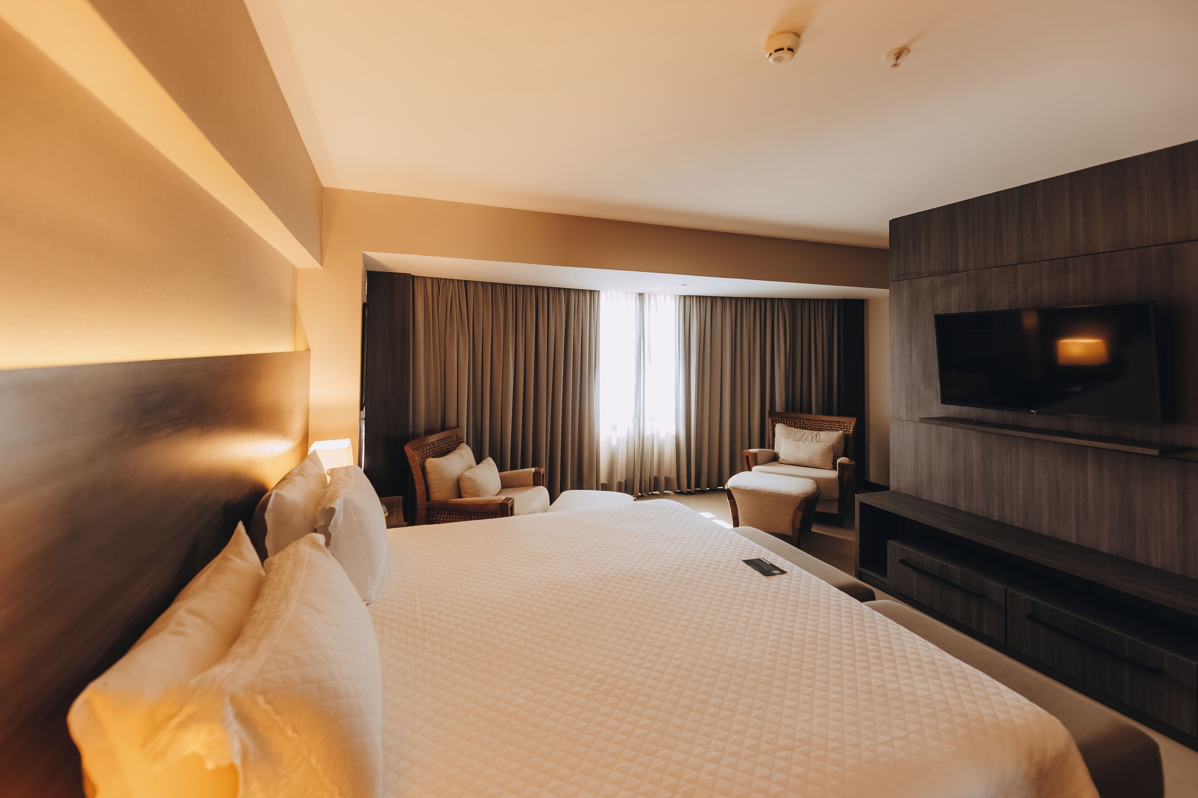 Habitación de hotel con una cama grande, un televisor montado en la pared y una zona de estar con sillas y una mesa.