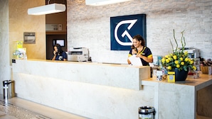 A reception desk with a modern design, a large logo on the wall, and a potted plant with yellow flowers. - Golden Tulip Natal Ponta Negra (Natal)