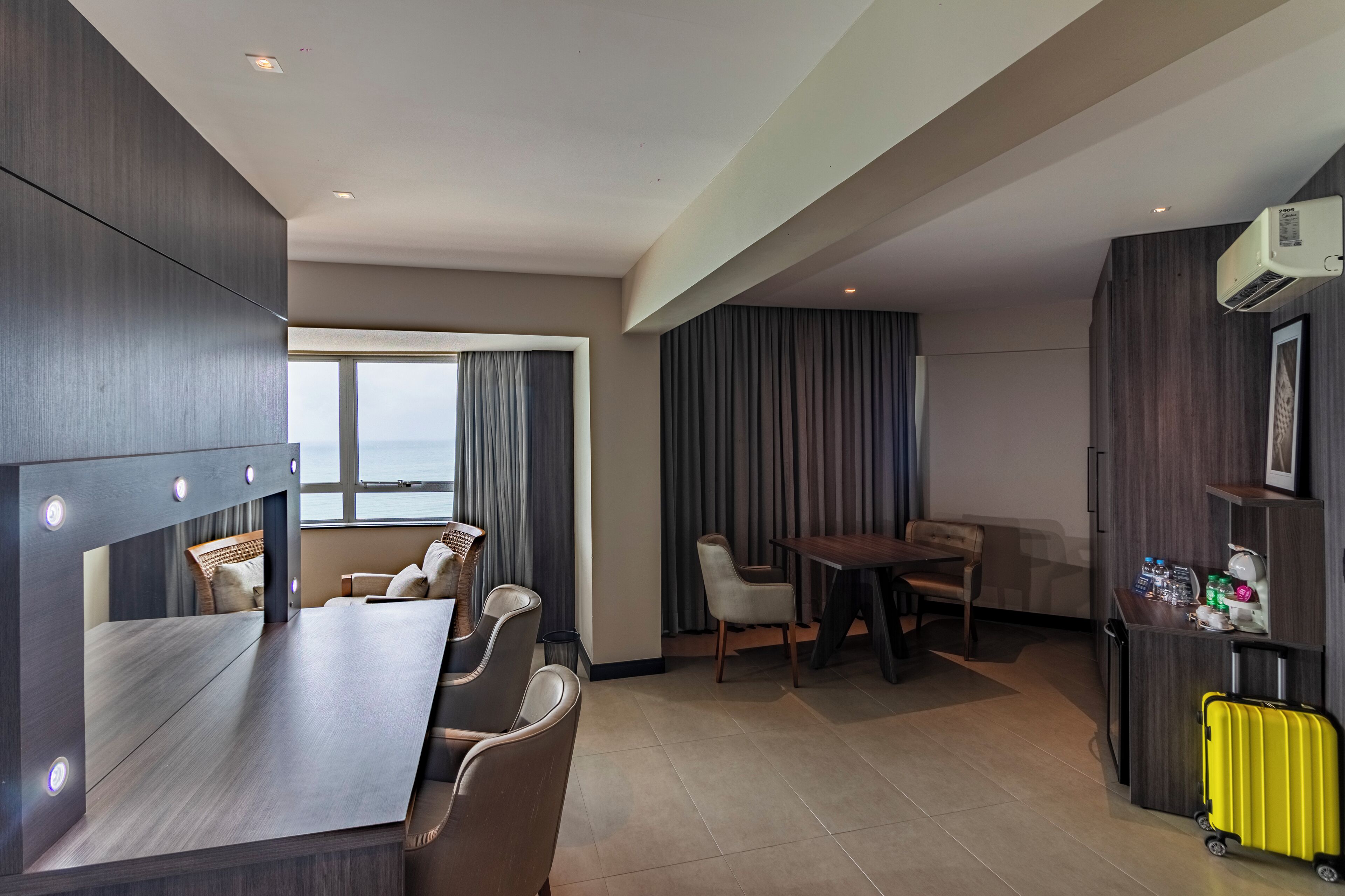 A hotel room with a large bed, a desk, a dining area, and a view of the outdoors.
