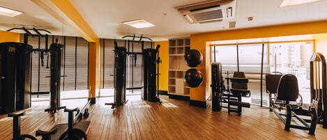 A gym with exercise equipment, wooden flooring, and large windows.