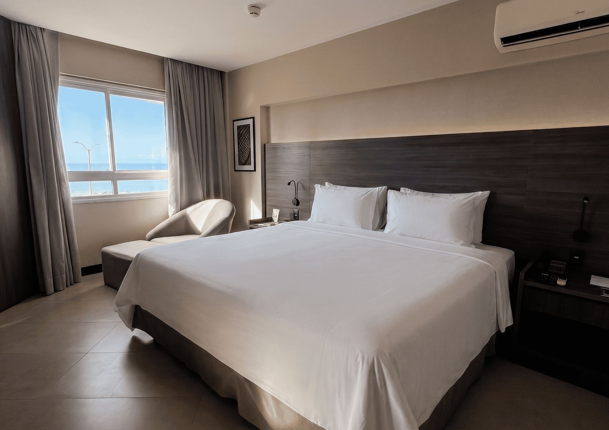 Una habitación de hotel con una cama grande, una silla, una mesita de noche y un ventanal con cortinas.