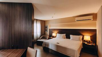 Habitación de hotel con una cama grande, un escritorio, una silla y un sofá. Hay un equipo de aire acondicionado en la pared y un cuadro colgado.
