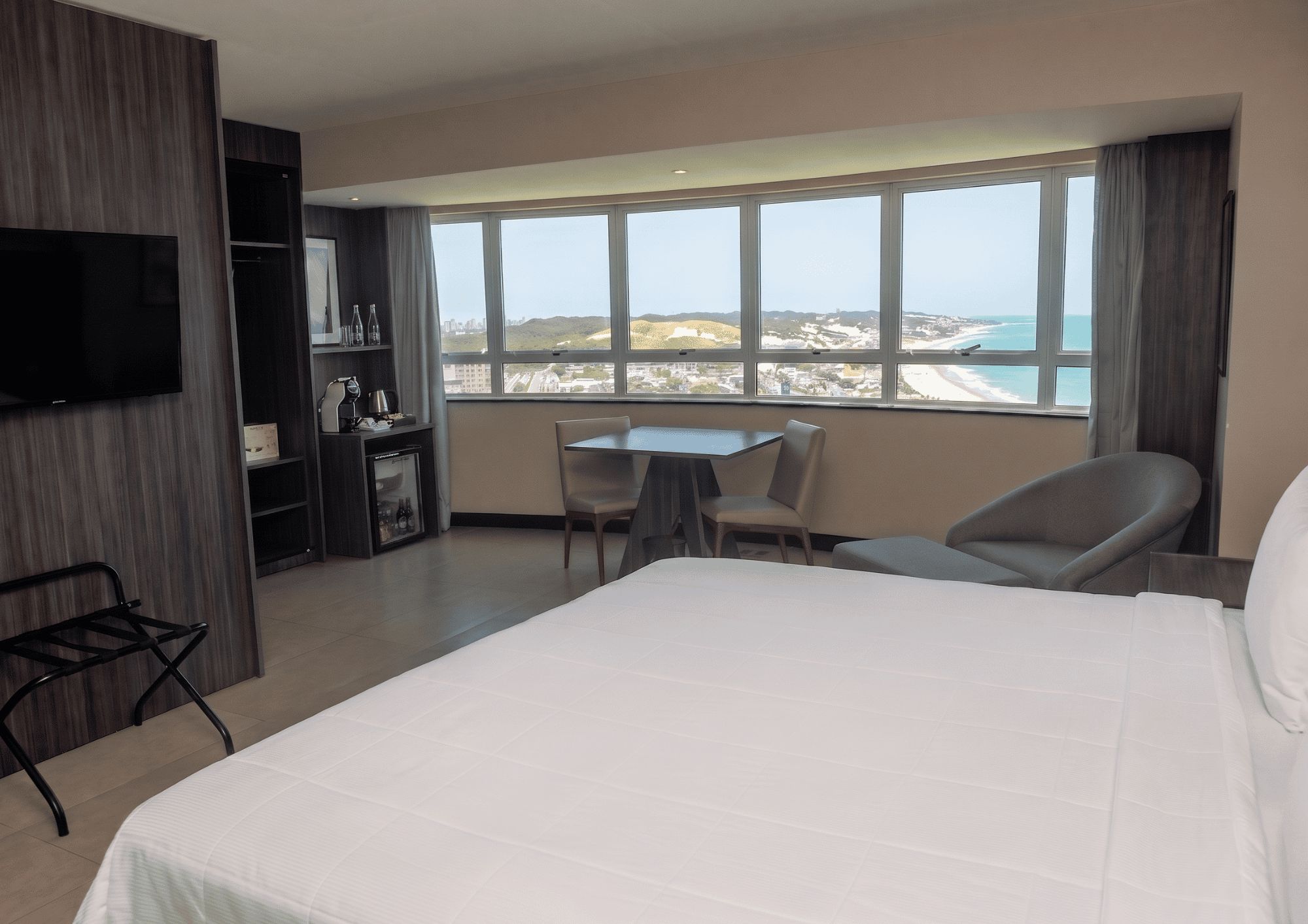 Une chambre d’hôtel avec un grand lit, un bureau, deux chaises, une télévision et une vue sur la plage.