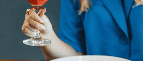 A person holding a glass of red drink, sitting at a table with a white plate of food.