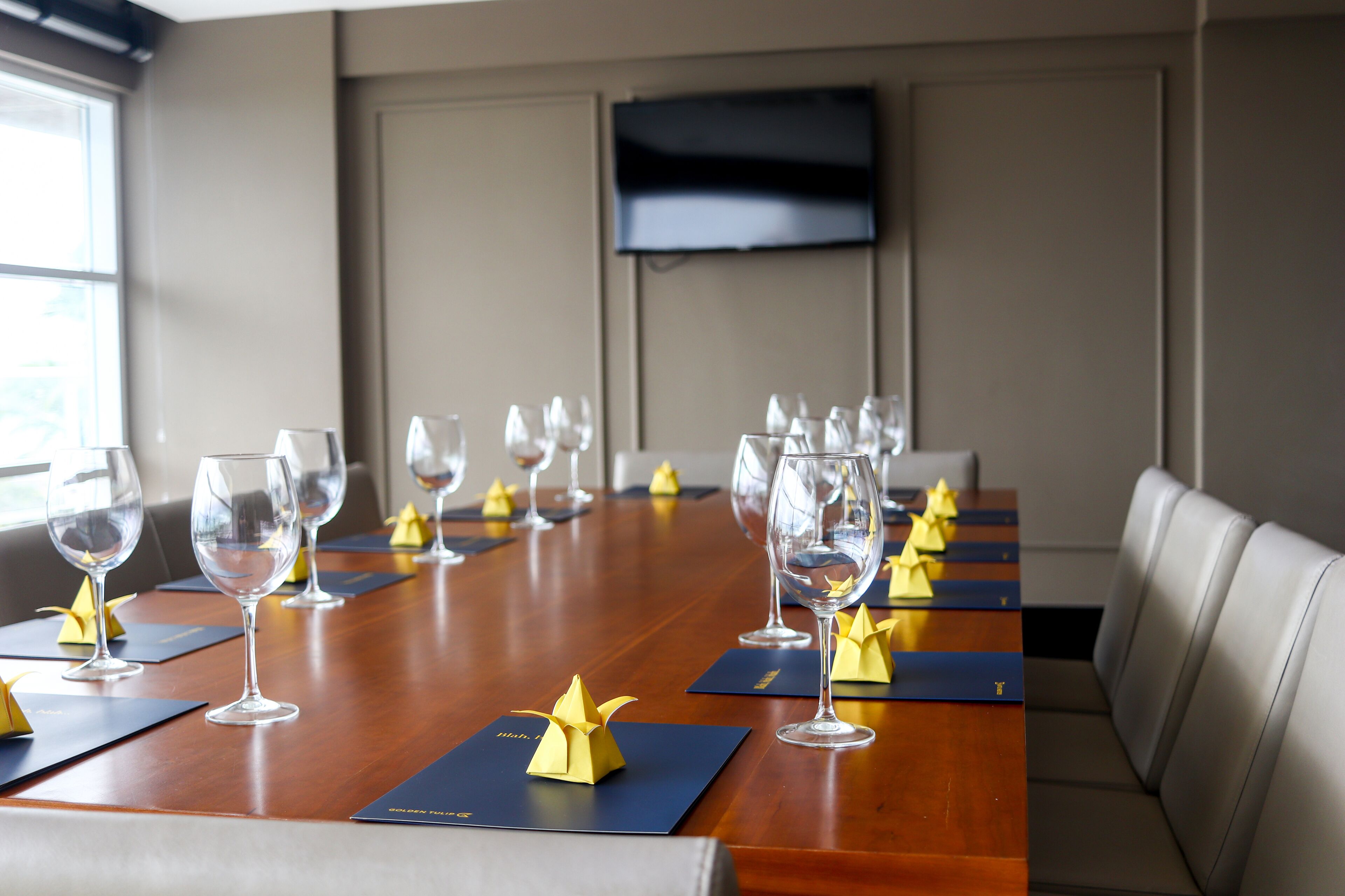Un salón de conferencias con una larga mesa dispuesta para una reunión, equipado con sillas y copas de vino.