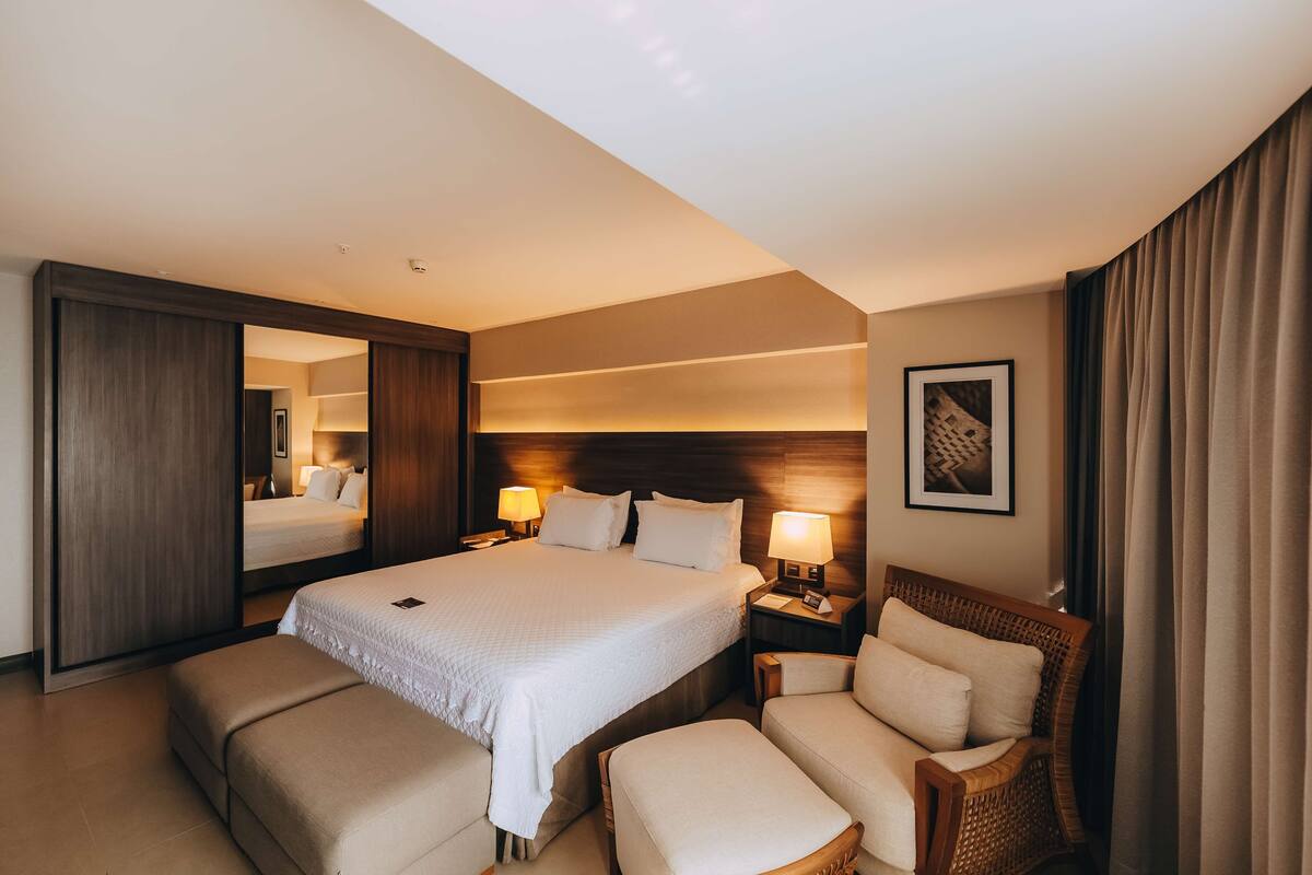 Ein Hotelzimmer mit einem großen Bett, zwei Nachttischen mit Lampen, einem Sessel und einem Spiegel.