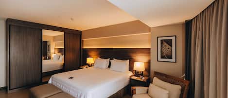 Una habitación de hotel con una cama grande, dos mesitas de noche con lámparas, una silla y un espejo.