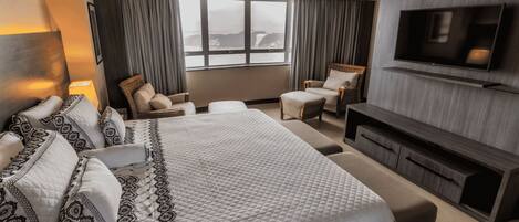 A hotel room with a large bed, two armchairs, a sofa, a TV, and a window with curtains.