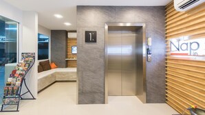 A modern reception area with a reception desk, a seating area, an elevator, and a wall-mounted sign. - Nap in Fest (Chiang Mai)