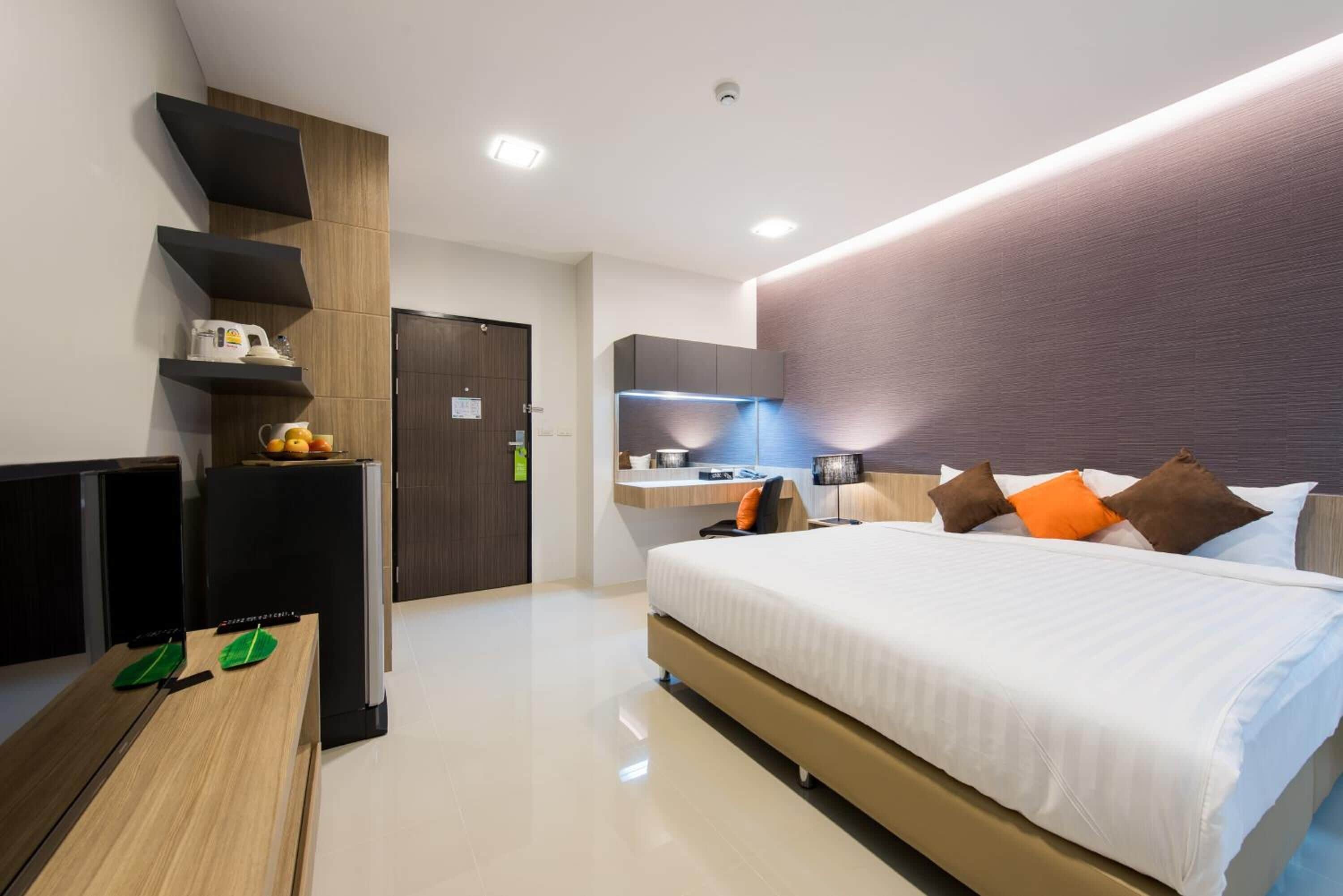 A modern hotel room with a large bed, a desk, a flat-screen TV, a kitchenette, and a bathroom.