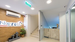 A reception area with a wooden wall, a reception desk, a staircase, and a potted plant. - Nap in Fest (Chiang Mai)
