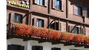 A multi-story building with a balcony adorned with red flowers. - Hotel Edelweiss (Courmayeur)
