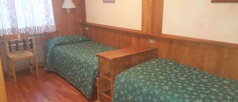 Una habitación pequeña y acogedora con dos camas individuales, una silla de madera, una mesita y una lámpara de pared.