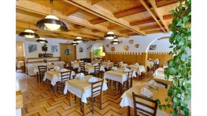 A restaurant with wooden ceiling beams, multiple tables with white tablecloths, and hanging pendant lights. - Hotel Edelweiss (Courmayeur)