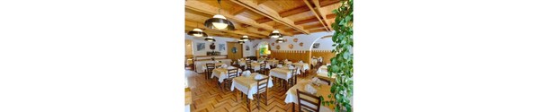 Un restaurante con vigas de madera en el techo, varias mesas con manteles blancos y lámparas colgantes.