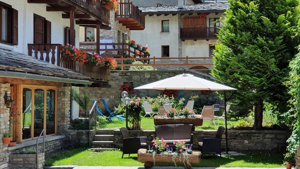 A courtyard with outdoor seating, stone walls, and a wooden staircase leading to a balcony with flower boxes. - Hotel Edelweiss (Courmayeur)