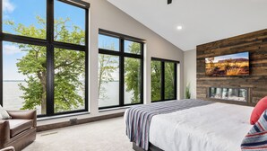 Une chambre avec de grandes fenêtres, un lit, une télévision et une cheminée.