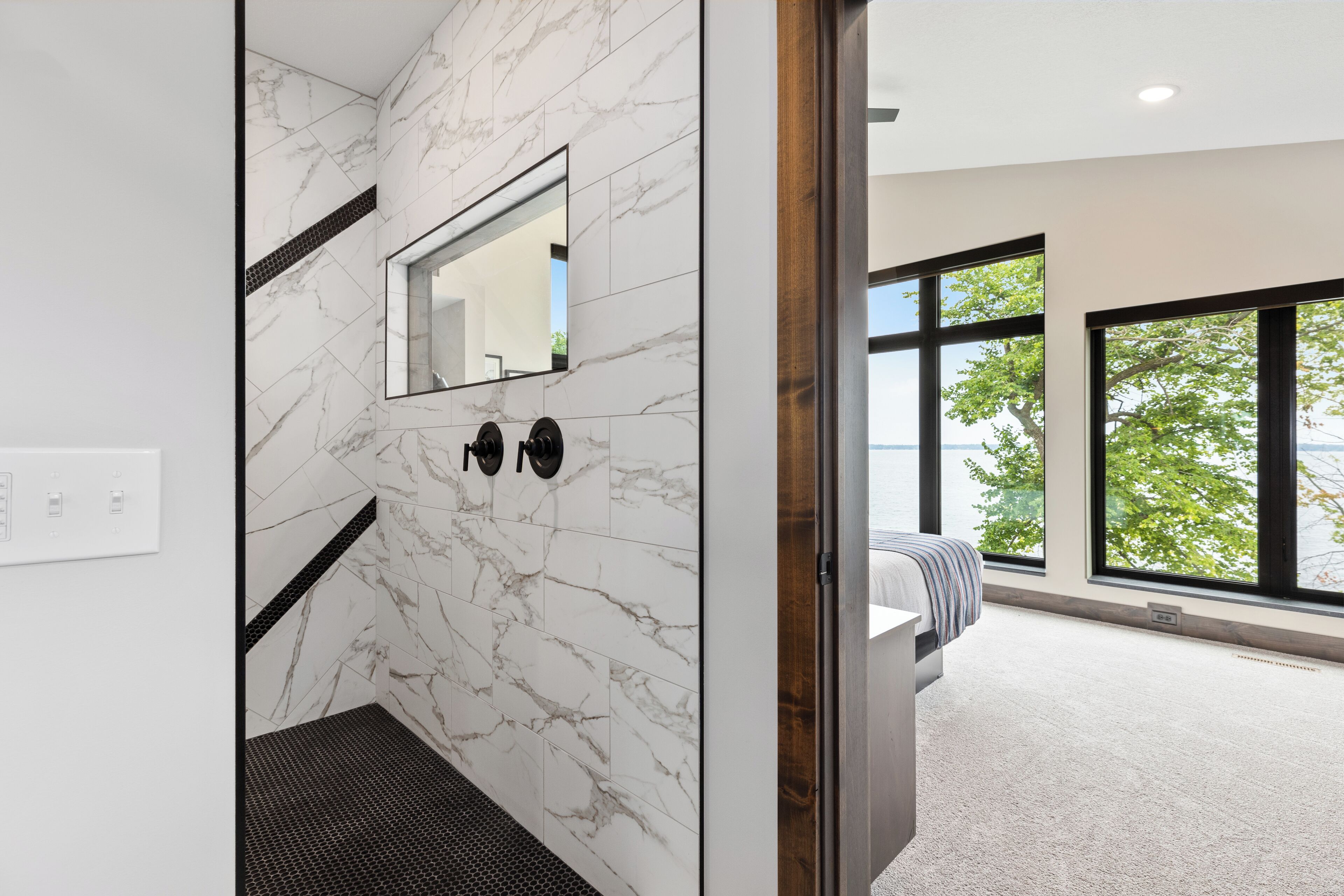 Une salle de bain moderne avec des murs en marbre, un grand miroir et une vue sur l’extérieur grâce à de grandes fenêtres.