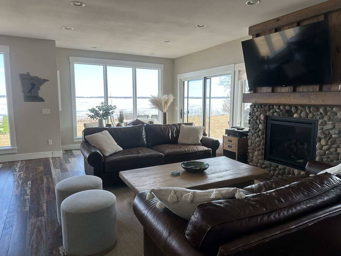 A spacious living room with a large television, a stone fireplace, and a view of the outdoors.