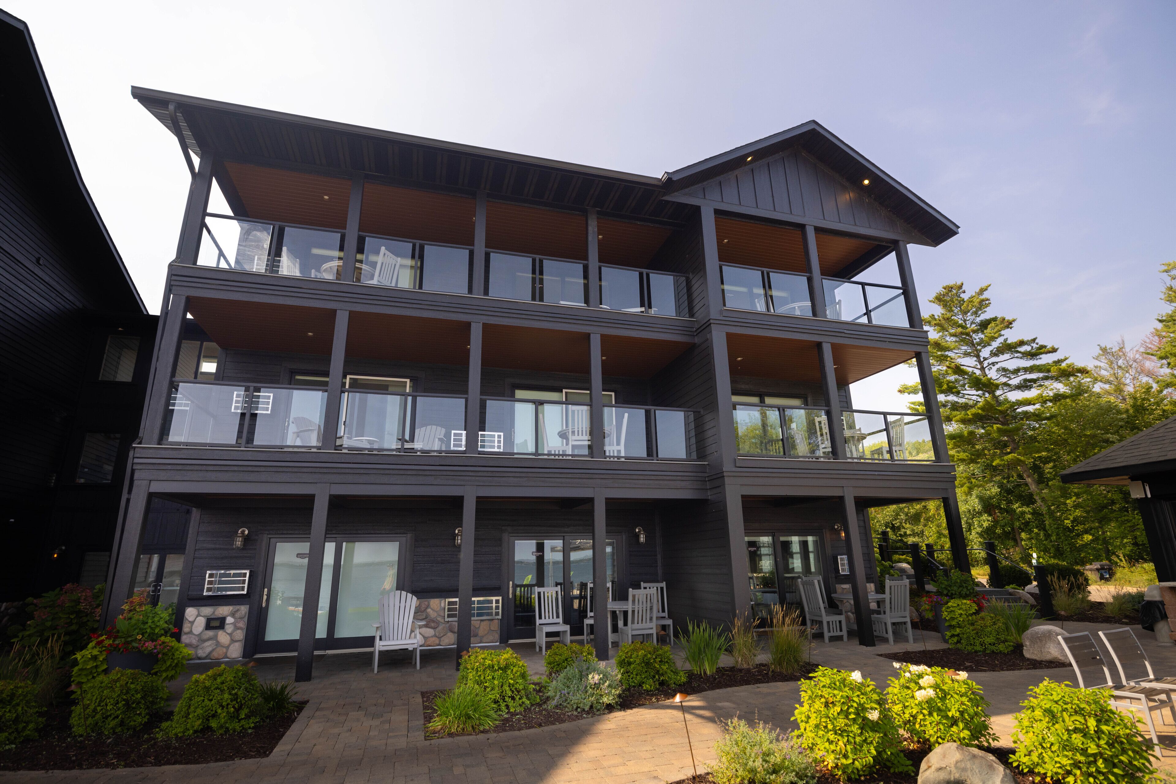 A modern two-story building with a balcony, stone accents, and outdoor seating.