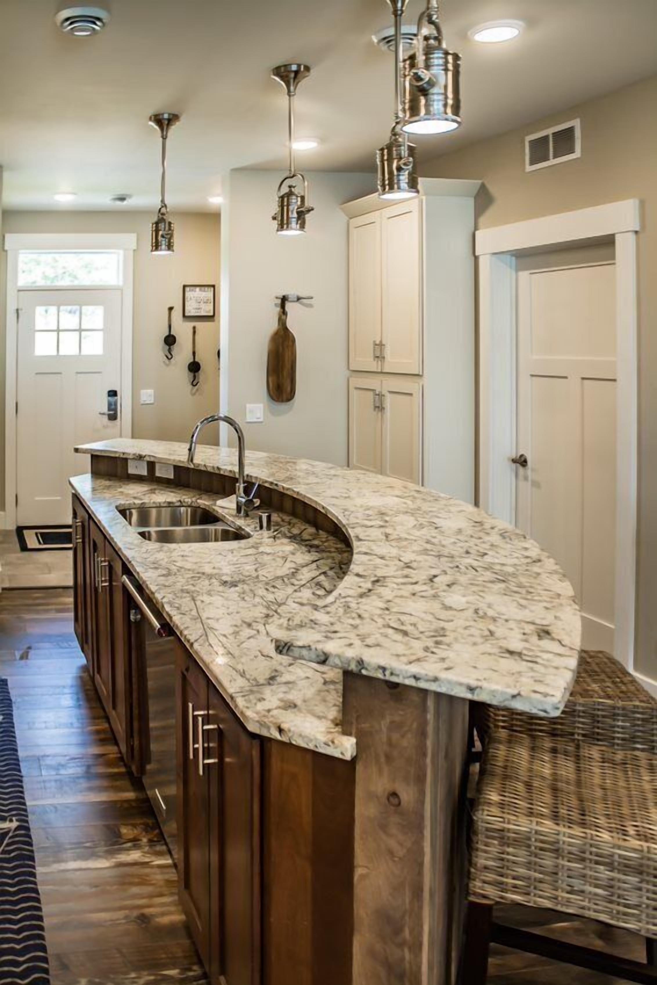 A kitchen with a curved island, stainless steel sinks, and pendant lighting.