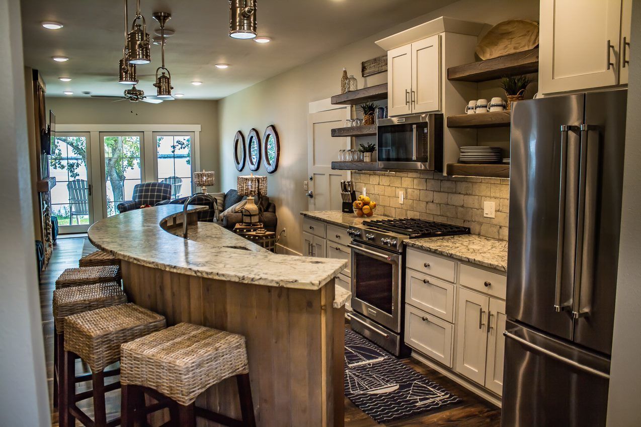 A modern kitchen with a curved island, stainless steel appliances, and a view to the outdoors.