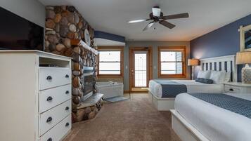 A bedroom with a stone wall, a flat-screen TV, a ceiling fan, a bathtub, and two beds.