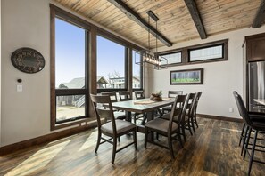 A dining area with a large table, chairs, and a view through large windows.