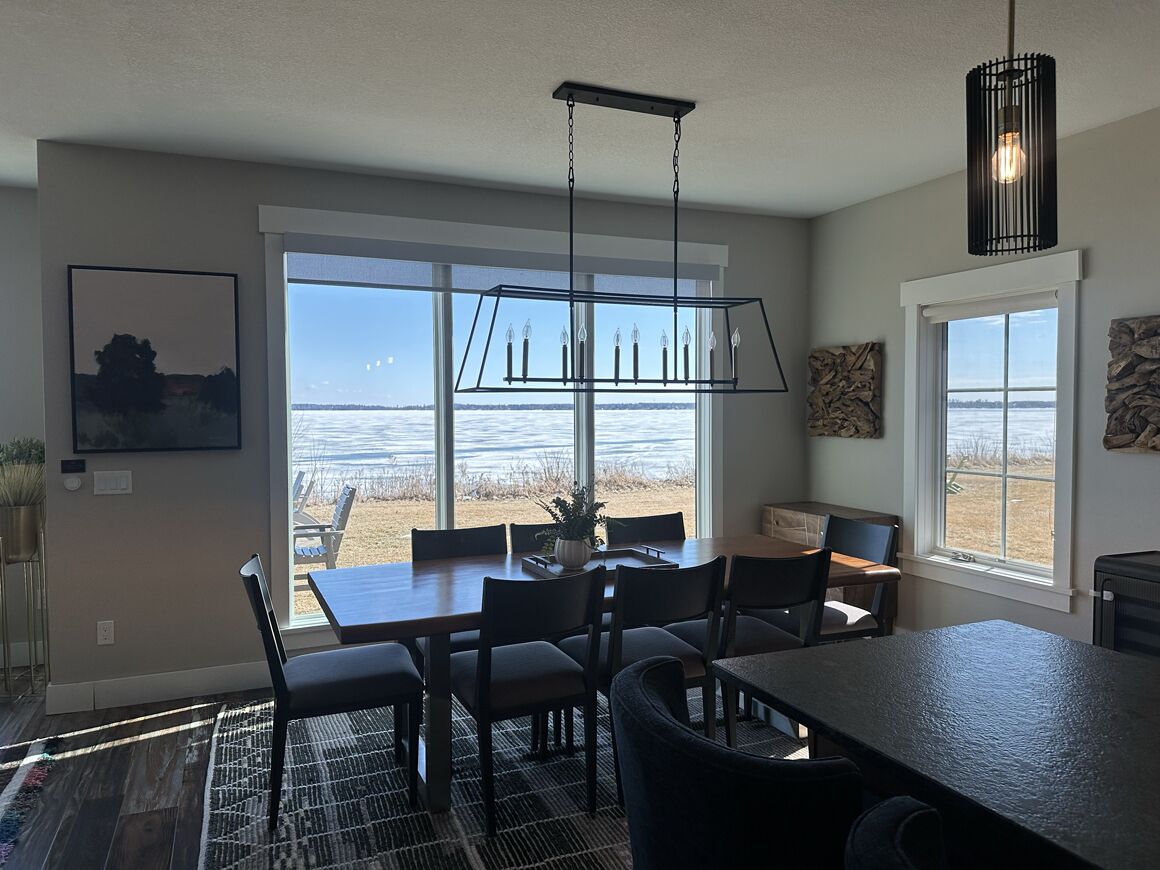Cozinha moderna com uma grande mesa de jantar, luminária pendente e vista para a praia.